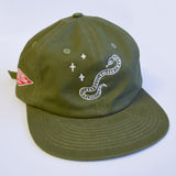An olive green baseball cap featuring a white embroidered snake and plus-sign graphic on the front, with a red diamond patch on the side, set against a plain white background.
