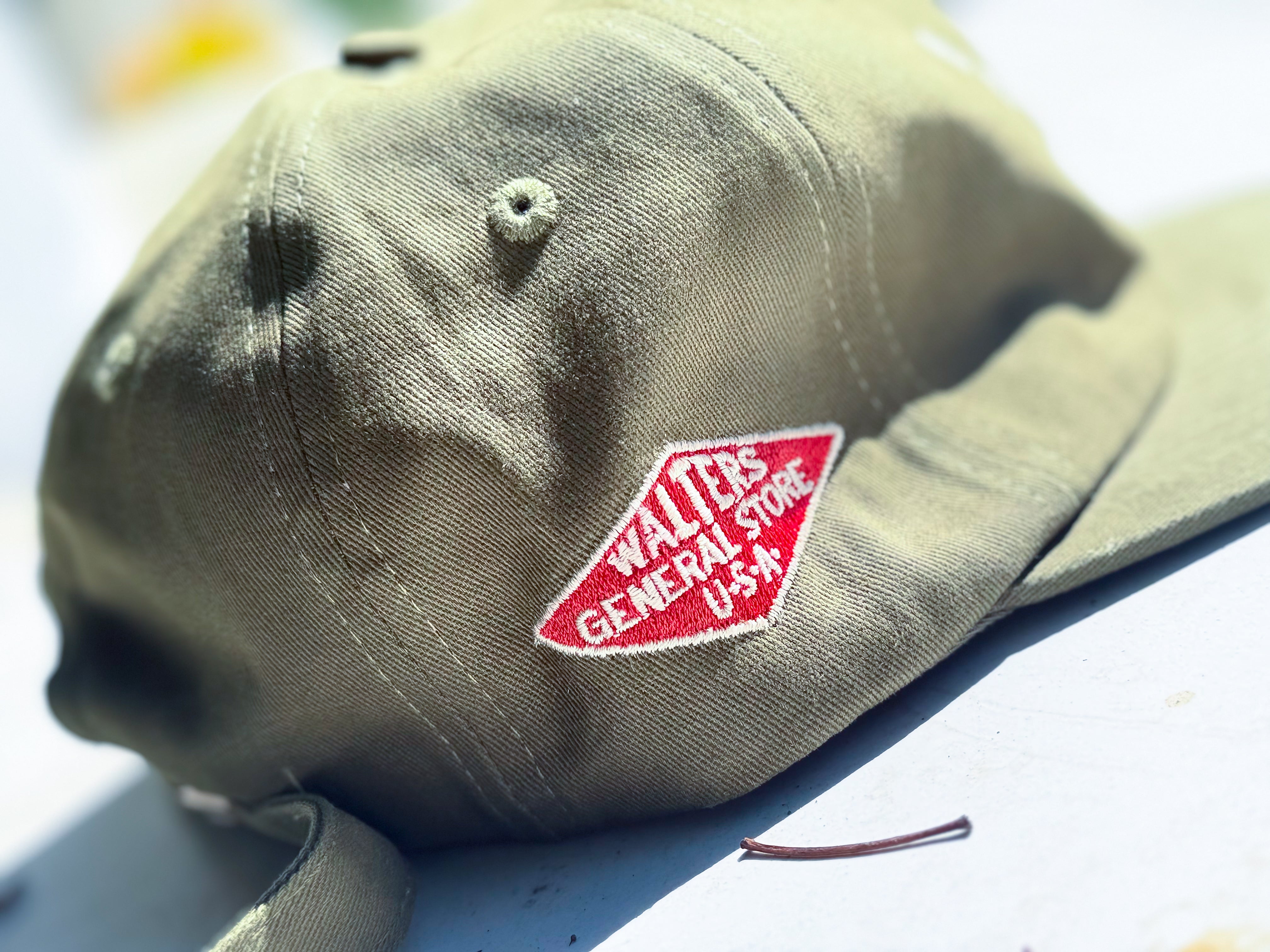 An olive green baseball cap with a red embroidered patch reading 'WALTERS GENERAL STORE U.S.A