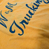 A close-up of a yellow fabric surface with dark blue cursive text reading "M & M Trucking" partially visible.