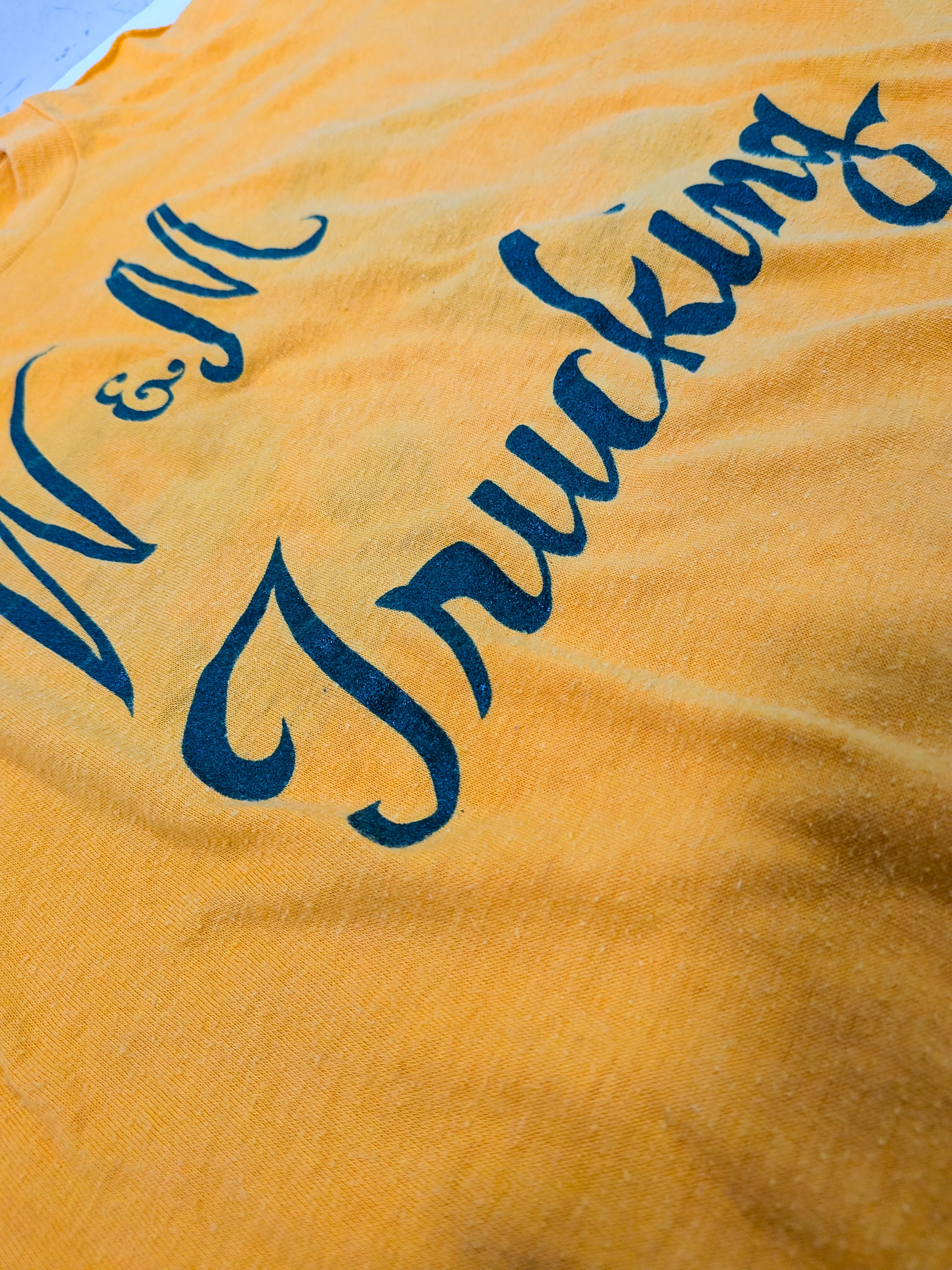 A close-up of a yellow fabric surface with dark blue cursive text reading "M & M Trucking" partially visible.