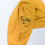 A folded mustard yellow t-shirt with a black printed graphic on the chest, displayed on a clean white background.