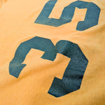A close-up of a yellow-orange fabric surface with a large dark green printed number 3.