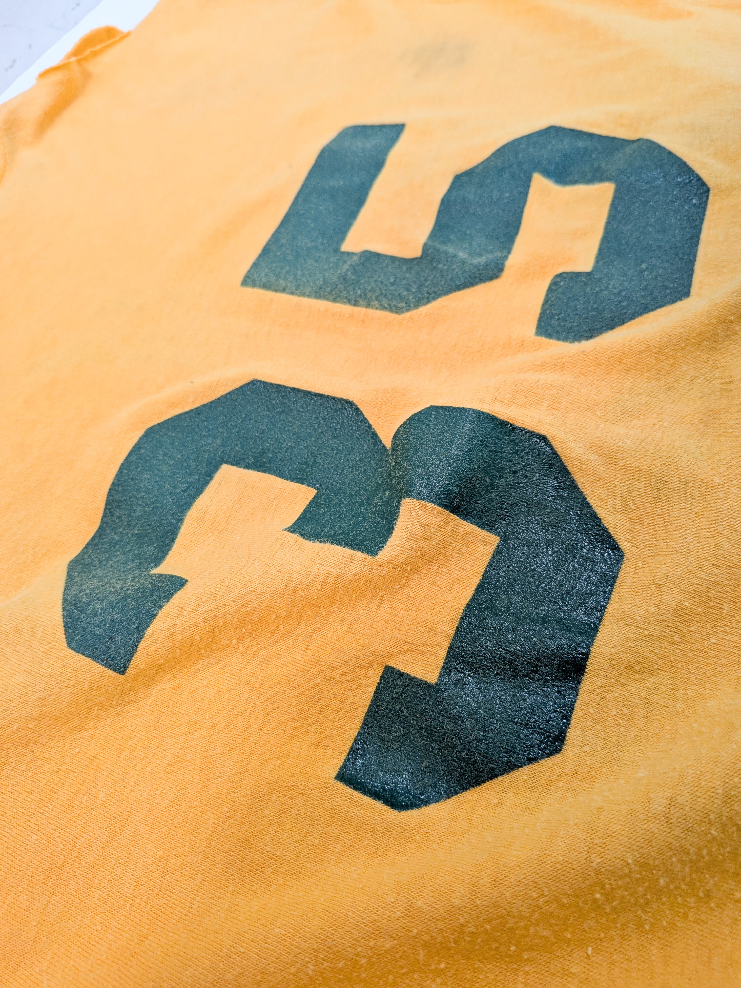 A close-up of a yellow-orange fabric surface with a large dark green printed number 3.