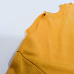A close-up of a mustard yellow knit garment, showing the shoulder seam and neckline against a plain white background.