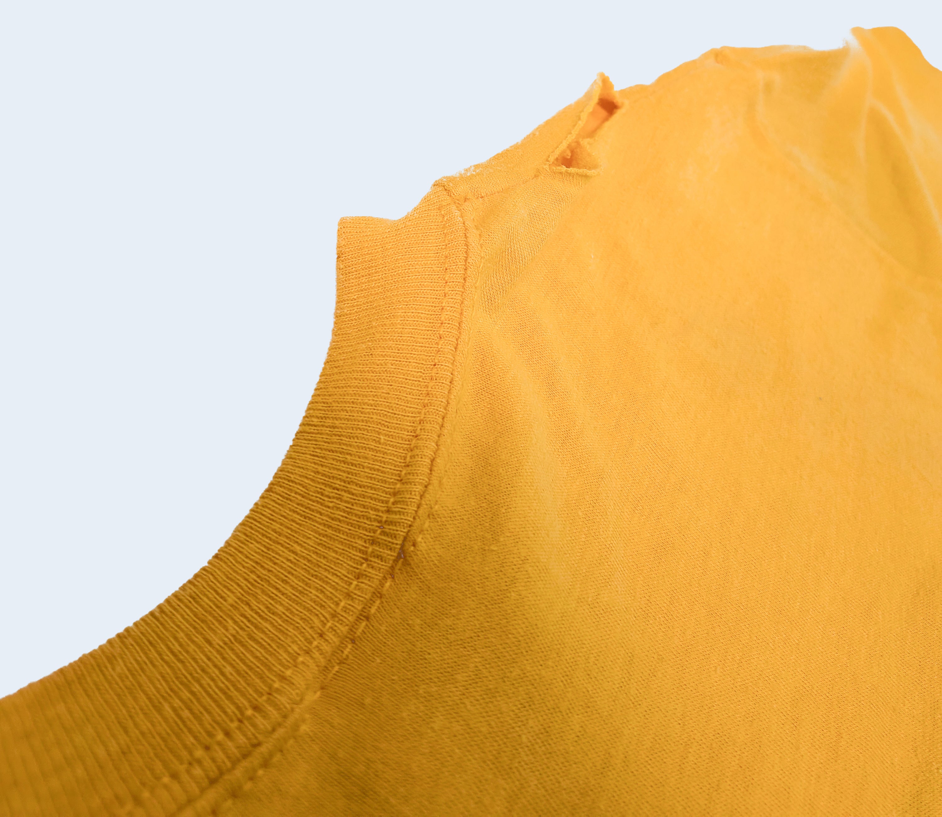 Close-up detail of a mustard yellow ribbed knit garment, showing the neckline and fabric texture against a light gray background.