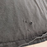 Close-up of a dark gray washed cotton fabric, showing a hemmed edge with visible frayed threads and small distressed holes in the knit texture.