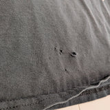 Close-up of a dark gray washed cotton fabric, showing a hemmed edge with visible frayed threads and small distressed holes in the knit texture.