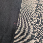 Close-up of a black knit garment featuring a cream-colored graphic print of the album 'Unknown Pleasures' wave pattern.