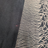 Close-up of a black knit garment featuring a cream-colored graphic print of the album 'Unknown Pleasures' wave pattern.
