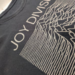 Close-up of a black Joy Division graphic t-shirt featuring the band's name and the 'Unknown Pleasures' line-art print.