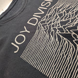 Close-up of a black Joy Division graphic t-shirt featuring the band's name and the 'Unknown Pleasures' line-art print.